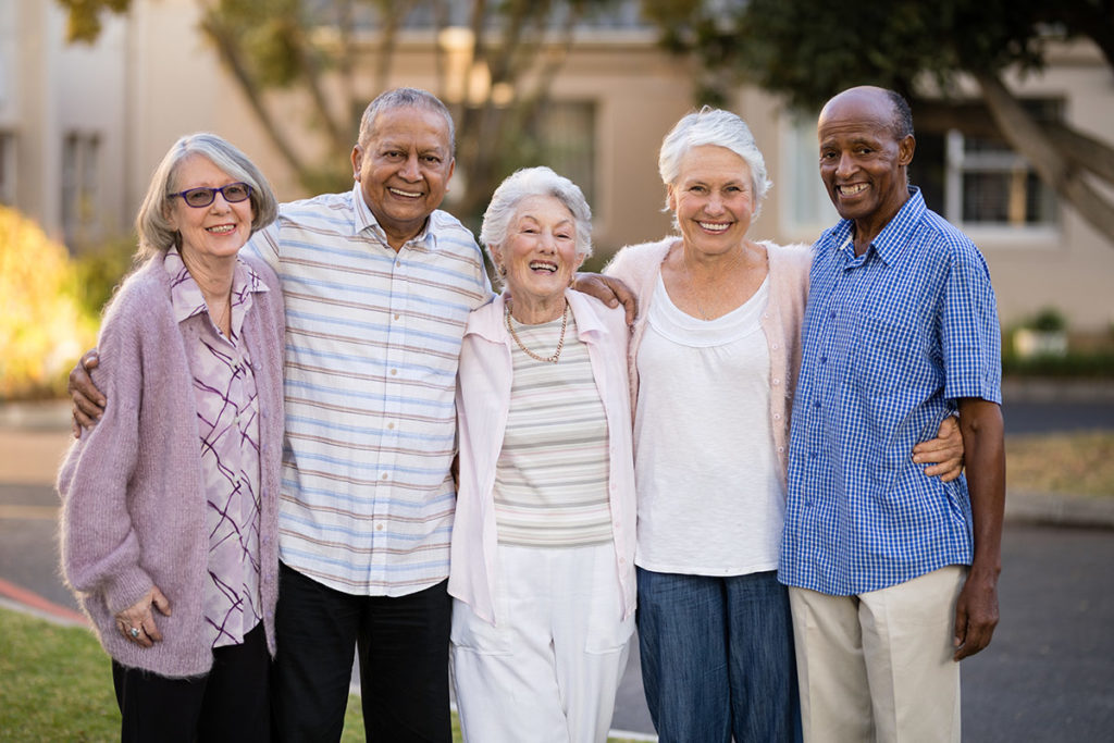 a photo of a diverse group of elder men and women standing closely together outdoors in what looks like a neighborhood