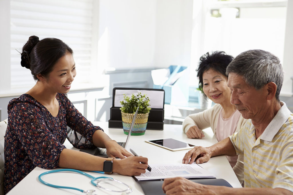 an image of a young woman talking to an elderly couple inside the young woman's brightly lit office going over paperwork